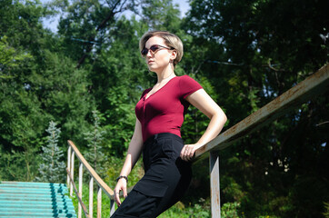 The girl leans on the railing of the ladder against the background of a green meadow and trees