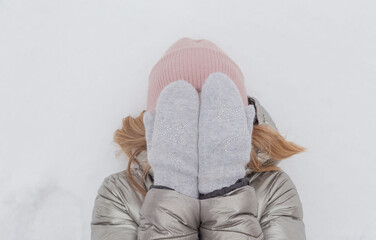 A beautiful blonde covers her face with her hands and lies in the snow. She is shy. Place for an inscription.