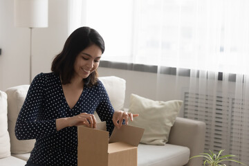 Smiling young mixed race vietnamese woman unpacking small cardboard box, satisfied with fast...
