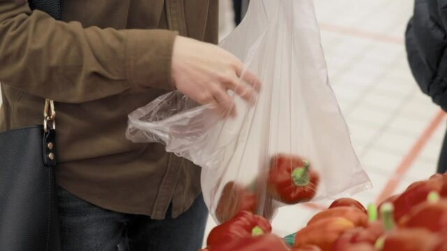 Female hands picking up red peppers in grocery market store, closeup handheld shot of girl putting red peppers into plastic bag 