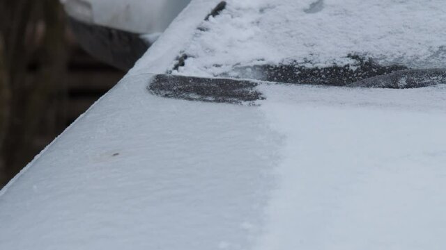 Person hand cleans ice from white electric vehicle hood with snow brush of yellow and black colours
