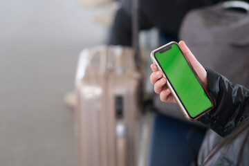 close up hand holding green screen phone, blur suitcase beside. Travel, journey, trip concept