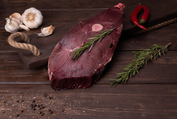 raw fresh meat on a wooden background. venison with red pepper and rosemary. garlic and seasonings....