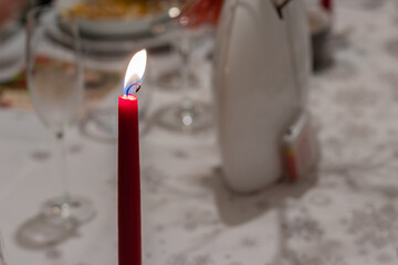 Red burning candle on a white tablecloth with utensils on the table for special occasions. 