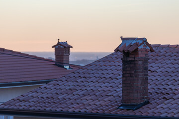 House roofs with chimneys with yellow sky sunset in the background.