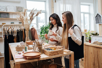 Close standing young women in an ecological shop choosing between various cosmetic products. Picking and checking item by item.