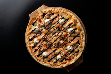 Smoked salmon pizza with small mozzarella balls, top view on black background