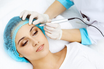 Professional beautician doing eyebrow tattoo at woman face. Permanent brow makeup in beauty salon, closeup. Cosmetology treatment