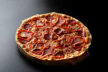 Huge hot meat pizza with melted cheese and bell pepper, single object on a black background