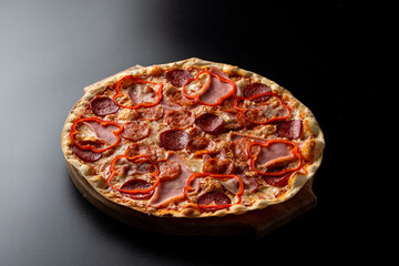 Huge hot meat pizza with melted cheese and bell pepper, single object on a black background