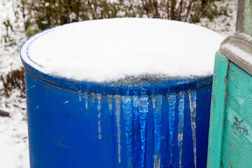 blue barrel in the garden with frozen ice with icicles