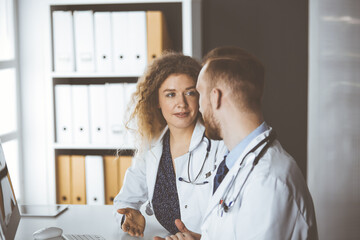 Red-bearded doctor with female colleague discussing current disease therapy while sitting at...