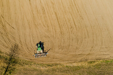 Aerial view large tractor cultivating a dry field. Top down aerial view tractor cultivating ground...