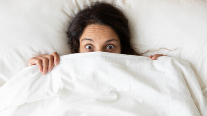Top view from above shocked surprised woman peeking from warm duvet, afraid of nightmares,...