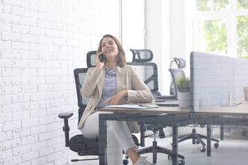 Photo through the glass of young smiling business woman using smartphone in office.