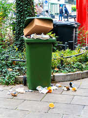 Trash spills out of an overfilled trash can on a pavement in the city