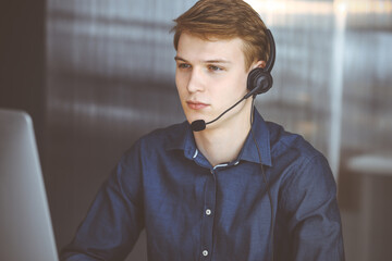 Young blond businessman using headset and computer at work. Startup business means working hard and out of time for success achievement