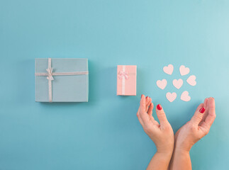 Gifts decorated with ribbon on blue background, woman hands hold small hearts. Flat lay, blue and pink present boxes, top view. Valentine, spring holidays, Christmas, birthday concept.