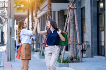 Two young women holding shopping bags are walking and happy while walking down the street,Sale,Consumerism and People Concept