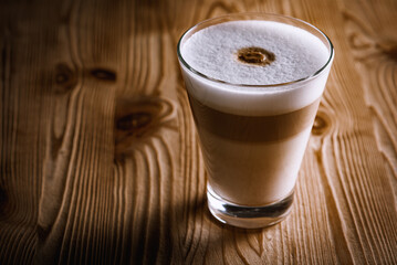 Cafe latte macchiato layered coffee in a glass coffee cup. The cup is on a wooden background. Dark background. Low key. Selective focusс