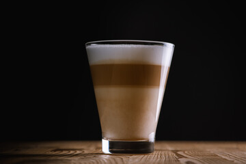Cafe latte macchiato layered coffee in a glass coffee cup. The cup is on a wooden background. Dark background. Low key. Selective focusс