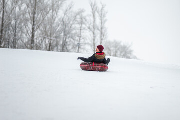Fototapeta na wymiar Active winter leisure. Tubing. A teenage boy rolls down a hillside in the woods on a tube.
