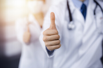 Unknown man-doctor and woman standing straight as a team and showing Ok sign with thumbs up in modern clinic. Medicine concept
