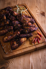 appetizing, golden chicken wings baked on the grill served on a wooden board, background with elements of fresh greens, top view. Dark background, low key