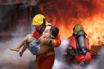 Firefighter holding child boy to save him in fire and smoke,Firemen rescue the boys from fire. - 404259432