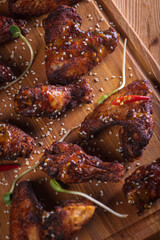 appetizing, golden chicken wings baked on the grill served on a wooden board, background with elements of fresh greens, top view. Dark background, low key