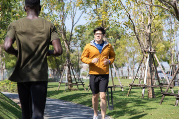 Fototapeta premium Asian Man in yellow hoodie jogging and running beside road in park at autumn morning.
