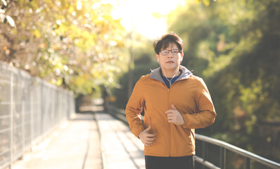 Obraz premium Asian Man in yellow hoodie jogging and running beside road in park at autumn morning.