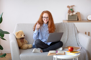Girl in glasses using laptop for elearning, sitting on couch