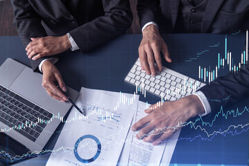 Two traders man and woman researching historic data to predict stock market behavior. Internet trading concept. Forex and financial hologram chart over the table with the documents