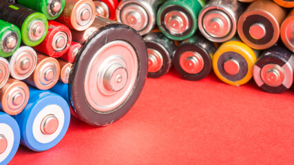Stack of used batteries on a red background. Batteries of different sizes