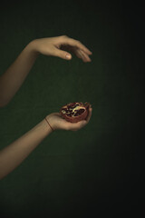 Female hands holding half a pomegranate on a green background