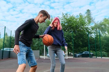 Teenagers guy and girl on an outdoor basketball court playing street basketball