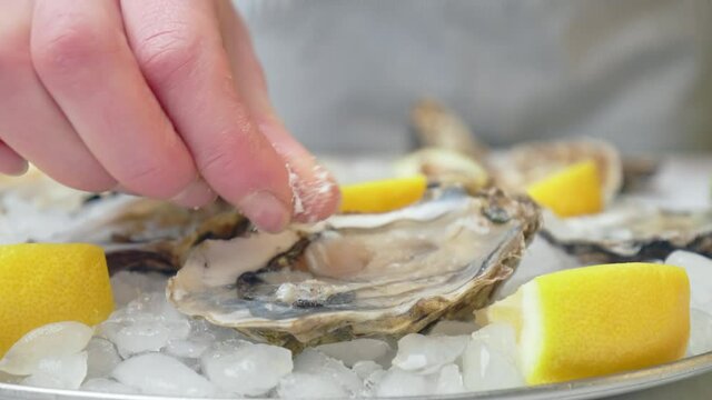 Close-up of a woman hand gently salting a fresh liquid-filled half-shell oysters. Concept of eating freshly opened from the shell oysters, way of serving seafood seashell in 4K.