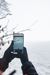 Frau fotografiert Winterlandschaft mit smartphone.