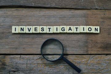 Top view of magnifying glass and alphabet letters with text INVESTIGATION over wooden background. 