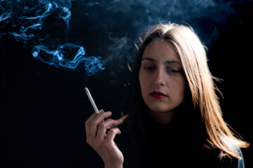 Obraz premium Young woman smoking cigarette on black background