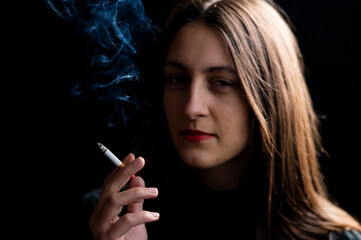 Obraz premium Young woman smoking cigarette on black background