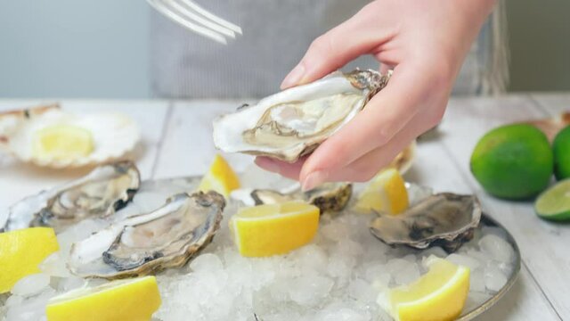 Close-up of a woman eating with a fork freshly opened oysters from crushed ice. Concept of serving oysters by seasoning with lemon juice and salting fresh liquid-filled half-shell, seafood in 4K.