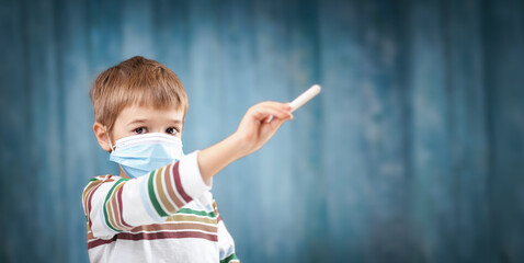 Boy in medical face protection mask indoors on blue background.
