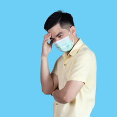 Stressful COVID-19 Coronavirus portrait handsome young asian .man wearing yellow shirt and mask protection from covid 19 isolated on blue background in studio. Asian man people. COVID-19 concept.
