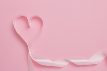 Pink ribbon in the shape of a heart on a pink background. Place for text. Valentine's day concept.