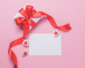 White blank sheet of paper and gift box on a pink background. Valentine's day concept.
