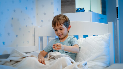 Fototapeta premium Portrait of cute toddler boy playing with toys in bed before going to sleep at night. Child playing with toys and having fun