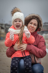 Fototapeta na wymiar Young mother holds her little daughter in her arms on the shore of the winter sea