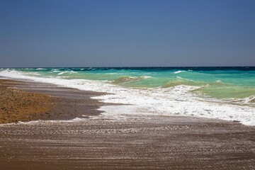 evocative image of a sandy beach with a sea of many colors and clear skies